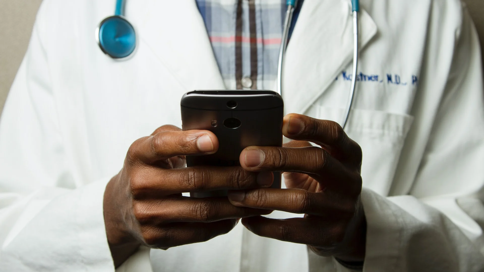 Doctor holding smartphone, only his hands and stethoscope hanging around his neck are in shot.webp Doctor holding smartphone, only his hands and stethoscope hanging around his neck are in shot.webp